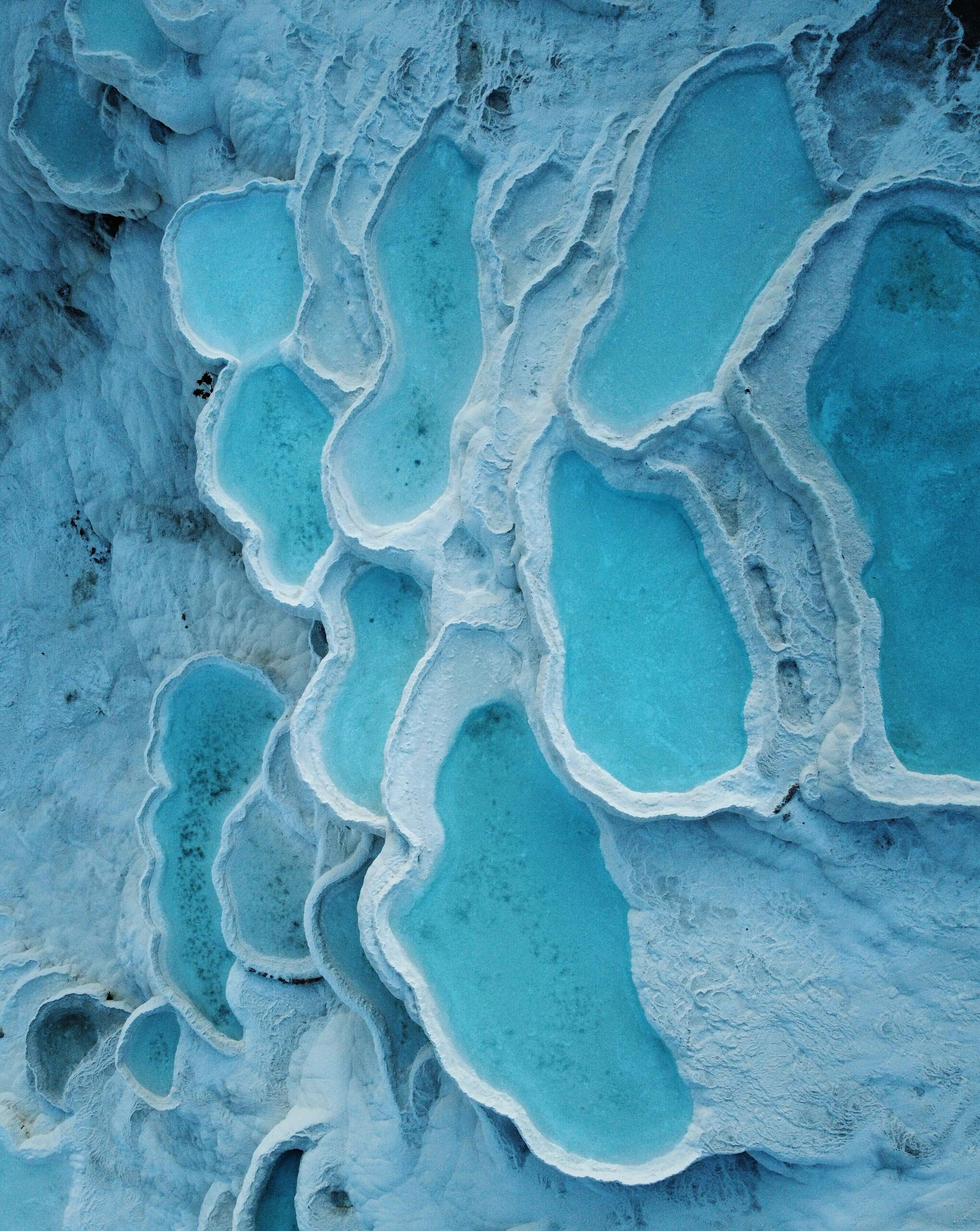 A stunning aerial view of natural turquoise hot springs pools among unique white limestone formations, showcasing nature's beauty.