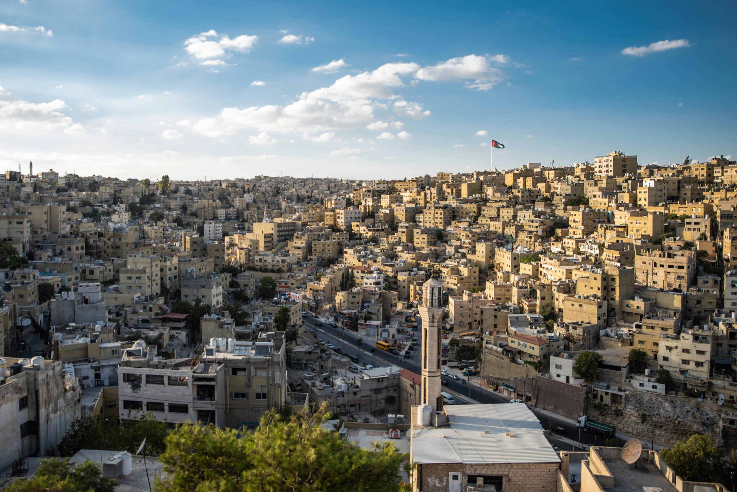 Aerial view of Amman's urban landscape with the Jordanian flag waving.