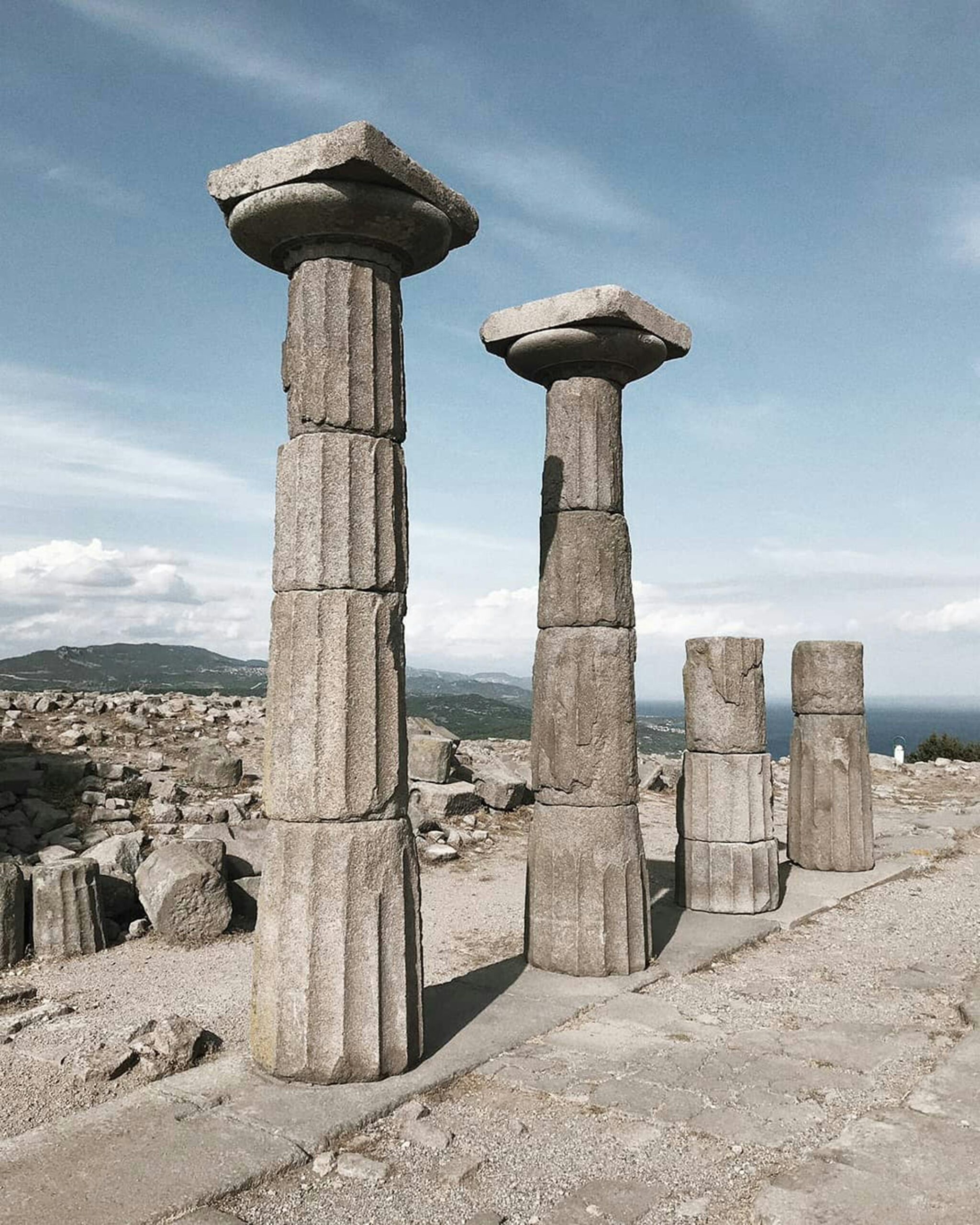 Ruins of ancient columns in Assos, Türkiye, under a blue sky.