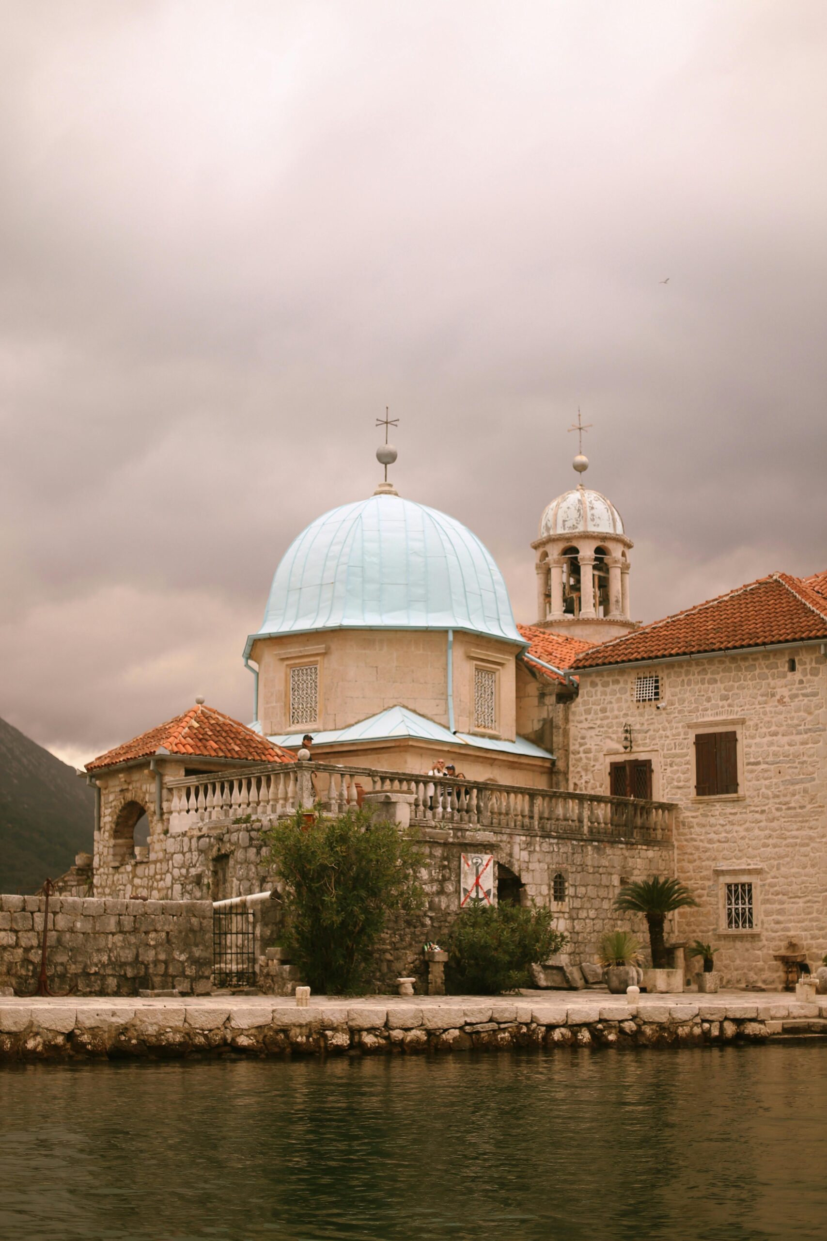 Calm scene of a historical stone church with a blue dome by the waterside under a cloudy sky.