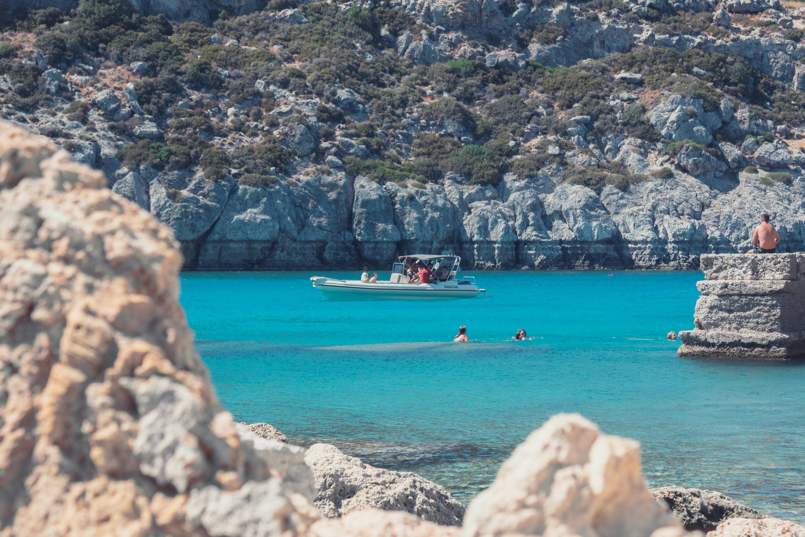 Enjoy a vibrant summer day in Rodos, Greece, with clear blue water and a boat amidst a stunning coastal landscape.
