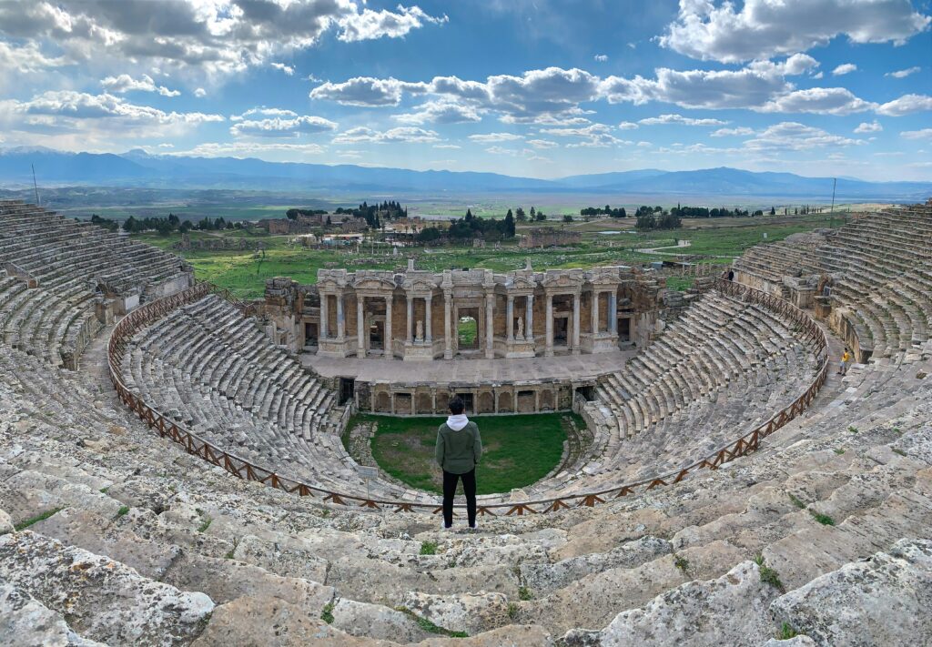 A man stands in the ancient Roman theater ruins in Hierapolis, Pamukkale, offering panoramic views.
