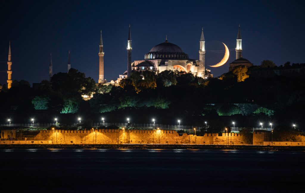 A stunning nighttime view of Hagia Sophia Grand Mosque in Istanbul with a crescent moon in the backdrop.