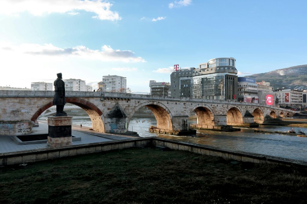 Iconic Stone Bridge in Skopje with urban skyline and statue under a clear blue sky.