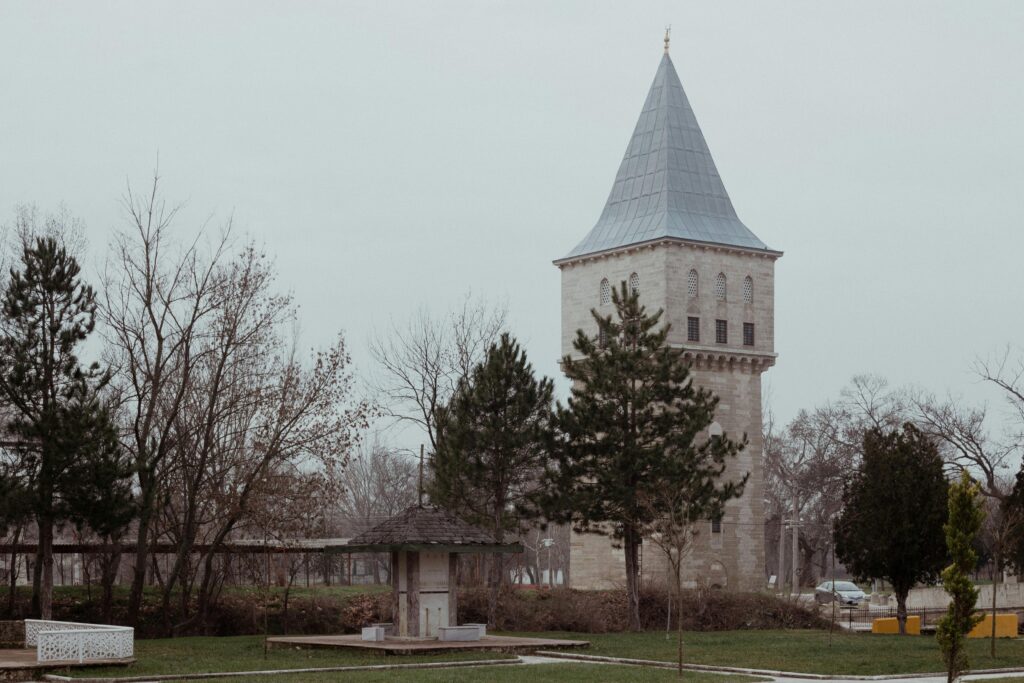 Serene winter scene of a historic tower in Edirne, Türkiye surrounded by trees.